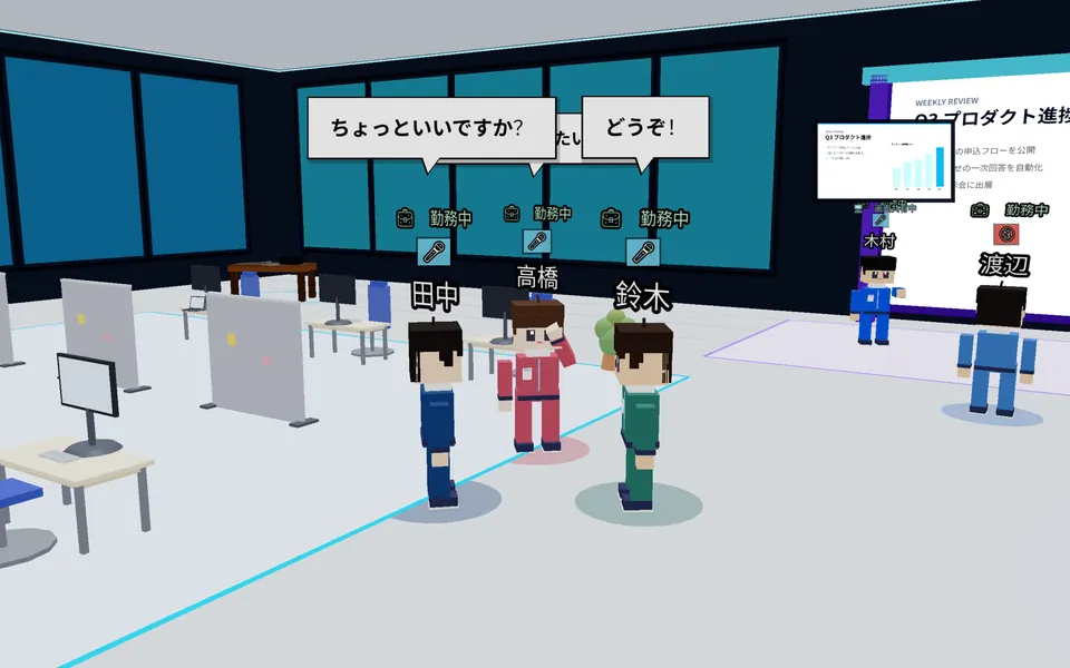 デスクの近くで3人が立ち話をしている。話している人の頭上のマイクのバッジが緑になっている